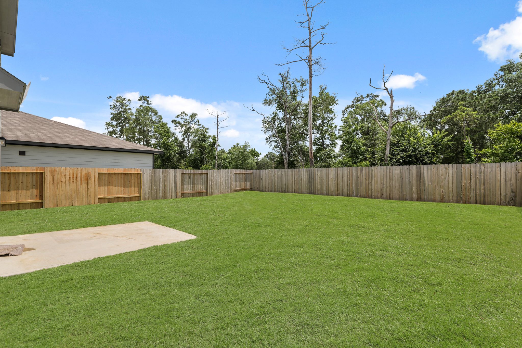 A fenced in yard with a wood fence and trees in the background.