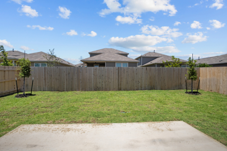 A fenced in yard with a wood fence and a house in the background.