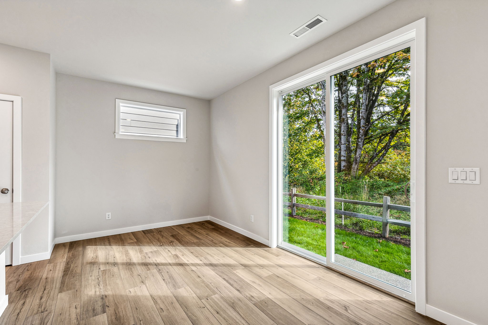 A room with a wood floor and a window with a view of trees.